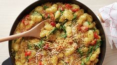 a skillet filled with pasta and vegetables on top of a wooden table next to a napkin