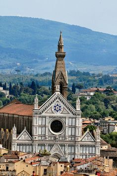 an old church in the middle of a city with mountains in the background and trees on either side