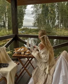 a woman sitting at a table on a deck with food and drinks in front of her