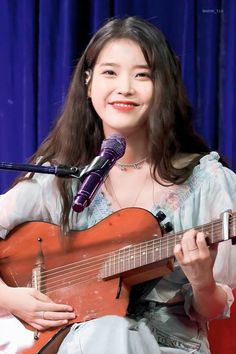 a woman holding a guitar while standing in front of a microphone