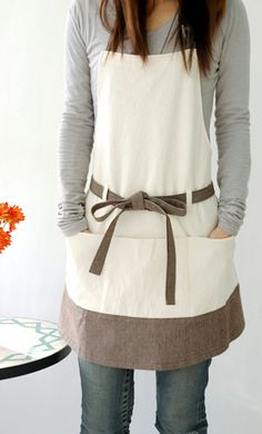 a woman wearing an apron standing in front of a vase with orange flowers on it