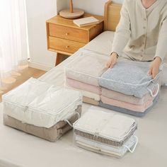 a woman sitting on top of a bed next to four folded blankets and two pillows