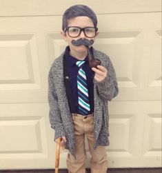 a young boy wearing glasses and a tie with a fake pipe in his mouth, standing next to a garage door