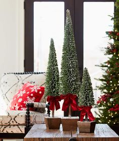 three small christmas trees sitting on top of a wooden table in front of a window