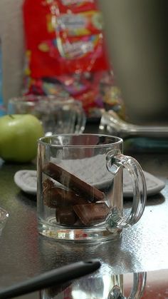 a glass cup filled with chocolate sitting on top of a table next to an apple