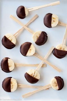 chocolate covered banana pops are arranged on a white plate with toothpicks sticking out of them