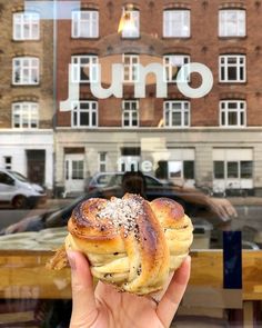 a person holding up a piece of bread in front of a building with the word uno on it