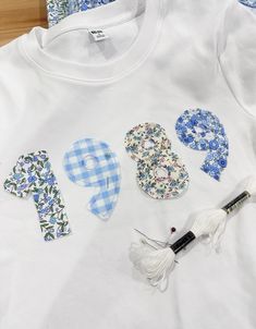 a white t - shirt with blue and white designs on it, scissors and thread