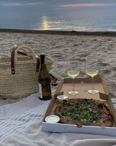 there is a pizza and two glasses of wine on the beach