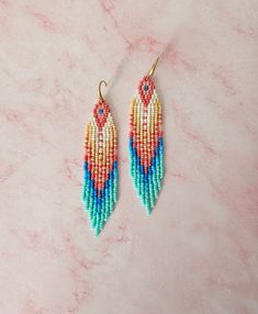 two pairs of beaded earrings on a marble surface with pink and blue colors in the background