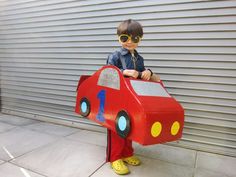 a young boy wearing sunglasses and standing in front of a cardboard firetruck costume