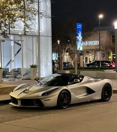 a silver sports car parked in front of a building at night with its lights on