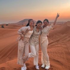 three women standing in the desert with their arms up and one holding her hand out