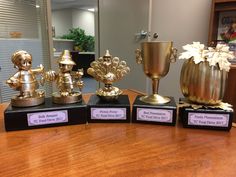 four trophies sitting on top of a wooden table in front of a glass vase and mirror