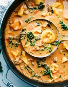 a ladle full of soup with dumplings and spinach on the side, ready to be eaten