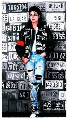 a man in ripped jeans standing next to a wall with license plates on the side