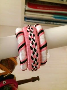 pink and black bracelets are hanging on a white pole in front of a stack of books