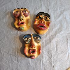 three ceramic masks with faces painted on them