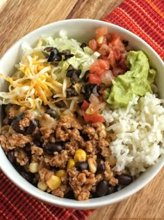 a white bowl filled with rice, beans and other food on top of a wooden table