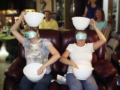 two women sitting on a brown couch with bowls in front of their eyes and people behind them