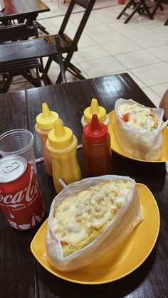 two yellow plates topped with food next to bottles of soda and ketchup on a table