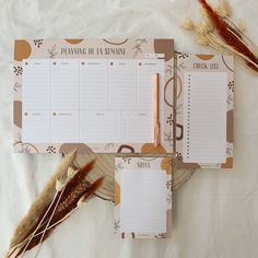 two planner pages on top of each other next to dried feathers and an orange pen