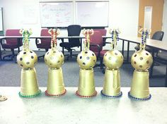 five golden vases sitting on top of a table in front of a whiteboard