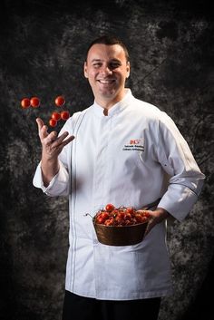 a man in chef's coat holding a bowl of tomatoes and two cherries