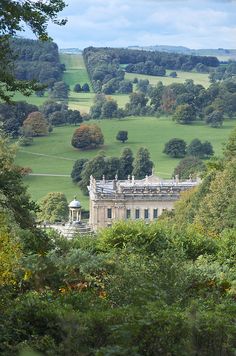 a large building in the middle of some trees and grass with hills in the background