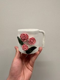 a hand holding a white coffee cup with pink roses on the outside and green leaves on the inside