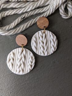 two white and gold earrings hanging from a rope on a gray surface next to some ropes