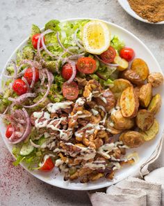 a white plate topped with salad and potatoes next to a bowl of seasoning on the side