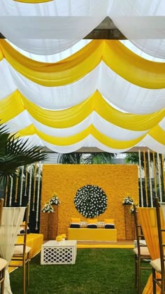 an outdoor wedding setup with yellow and white draping, flowers and greenery