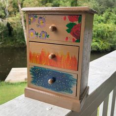 a painted dresser sitting on top of a wooden deck next to a river and trees