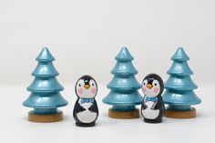 three small penguin figurines standing next to each other in front of christmas trees