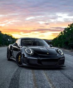 a black porsche sports car driving down the road at sunset with trees in the background