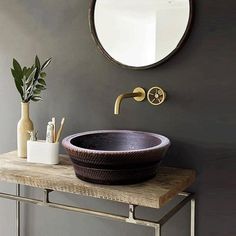 a bathroom sink sitting on top of a wooden counter next to a mirror and vase