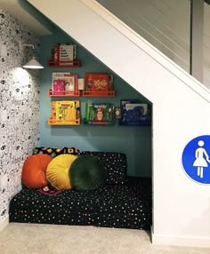 a child's playroom under the stairs with bookshelves and colorful pillows