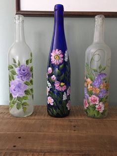 three painted glass bottles sitting on top of a wooden table next to a framed photo