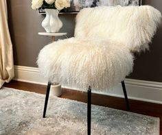 a white chair sitting on top of a rug next to a vase filled with flowers