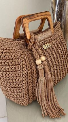 a crocheted brown purse with wooden handles and tassels on the handle