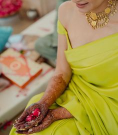 a woman in a yellow dress sitting down with her hands on her chest and wearing gold jewelry