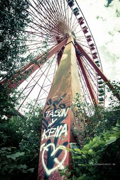 a large ferris wheel with graffiti on it's side in the woods next to trees