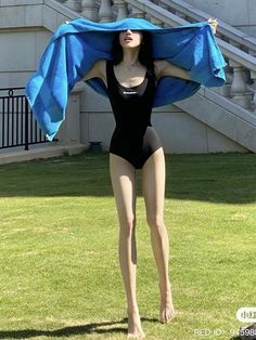 a woman in a black bodysuit is holding a blue cloth over her head while standing on the grass