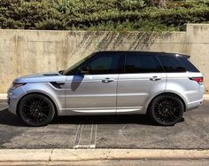 a silver range rover parked in a parking lot next to a concrete wall and shrubbery