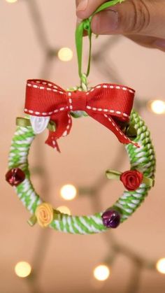 a hand holding a green and red wreath ornament with ribbon around it's center