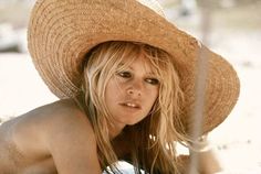 a woman wearing a straw hat on top of her head in the sand and looking at the camera