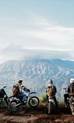 three men sitting on motorcycles in the mountains