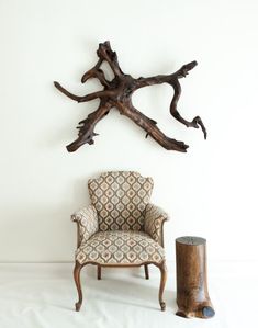 a chair sitting in front of a wall mounted tree branch sculpture on a white wall