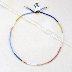 a multicolored beaded necklace is displayed on a white cloth with a tag